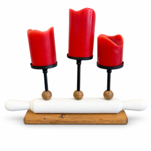 Decorative three-candle holder featuring red pillar candles, black metal stands, wood accents, and a white rolling pin design.