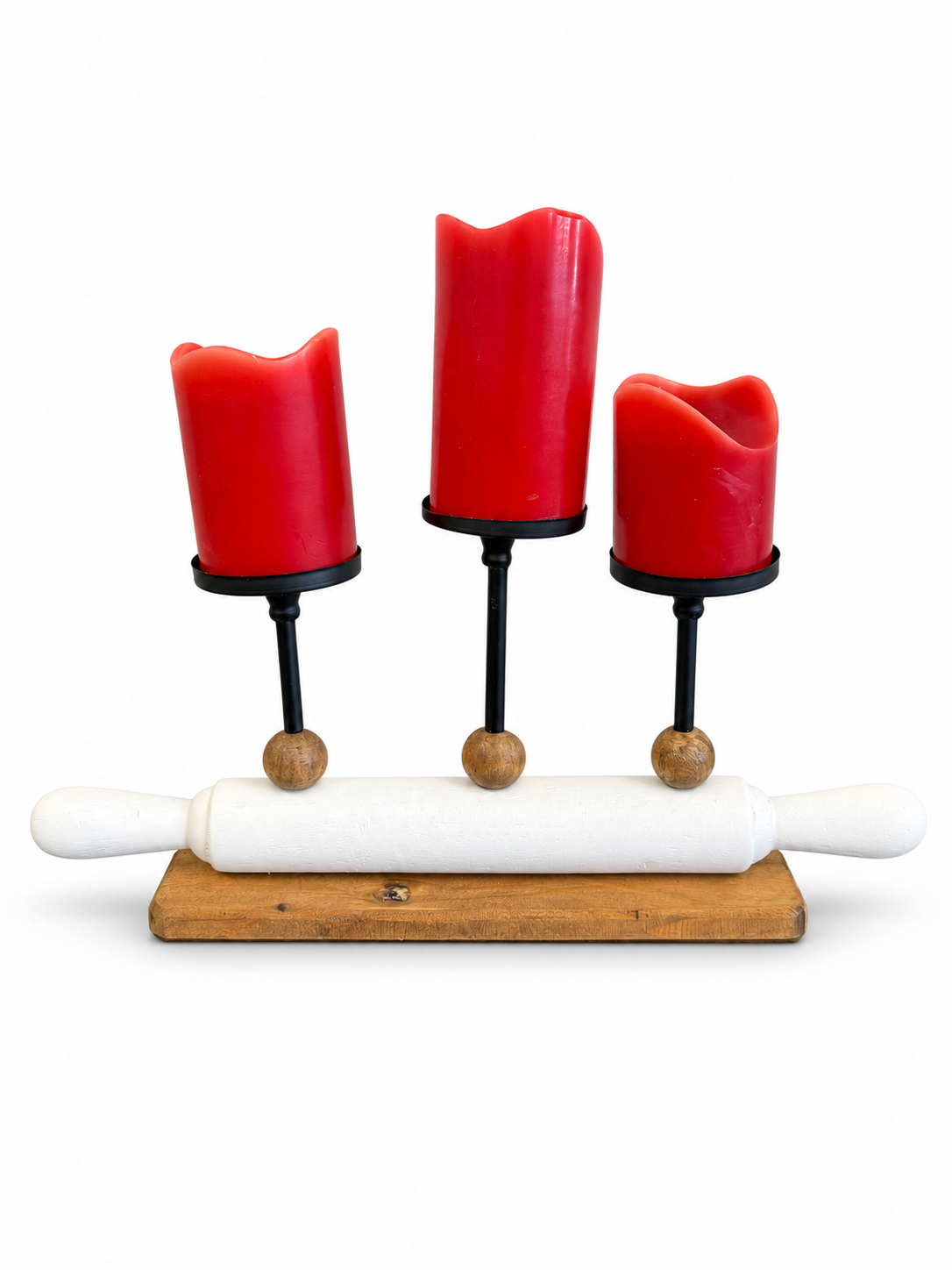 Decorative three-candle holder featuring red pillar candles, black metal stands, wood accents, and a white rolling pin design.