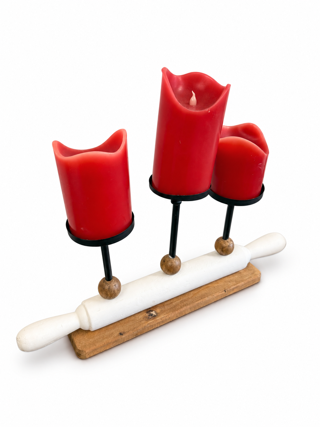 Decorative three-candle holder featuring red pillar candles, black metal stands, wood accents, and a white rolling pin design.